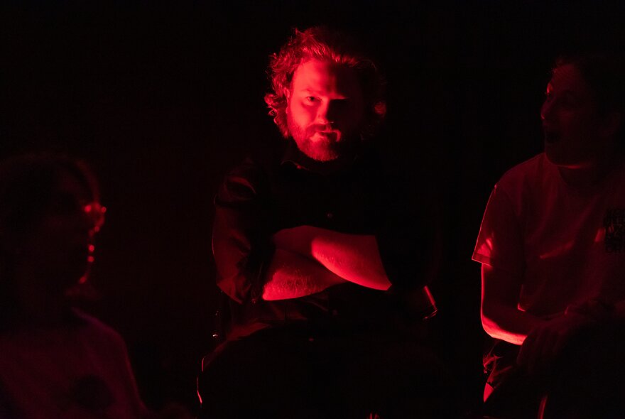 A man highlighted by a red light, standing with his arms crossed.