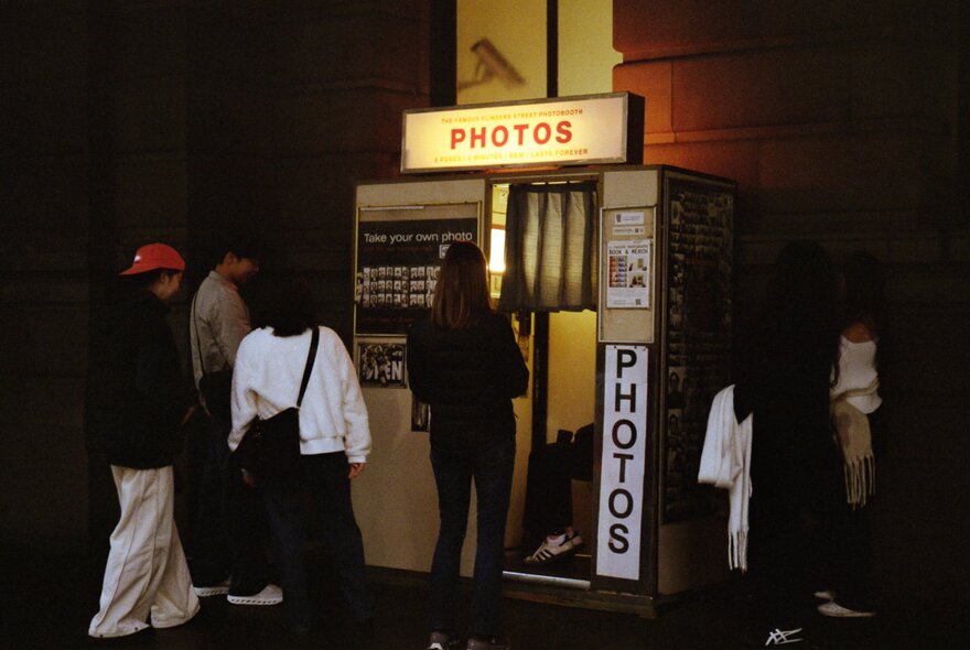 People lining up outside a retro photobooth at night.