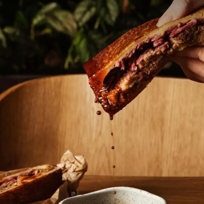 Hands holding a beef toastie dripping gravy.