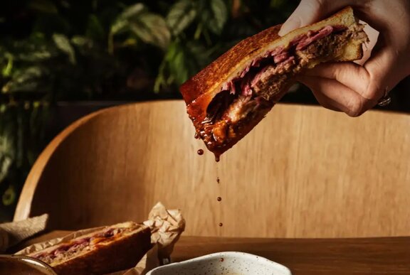 Hands holding a beef toastie dripping gravy.