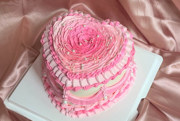 A vintage pink heart-shaped cake featuring intricate pink and white piped frosting details. 