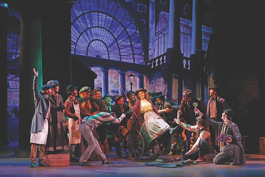 A scene from the musical My Fair Lady, with a large ensemble cast singing and dancing on stage.