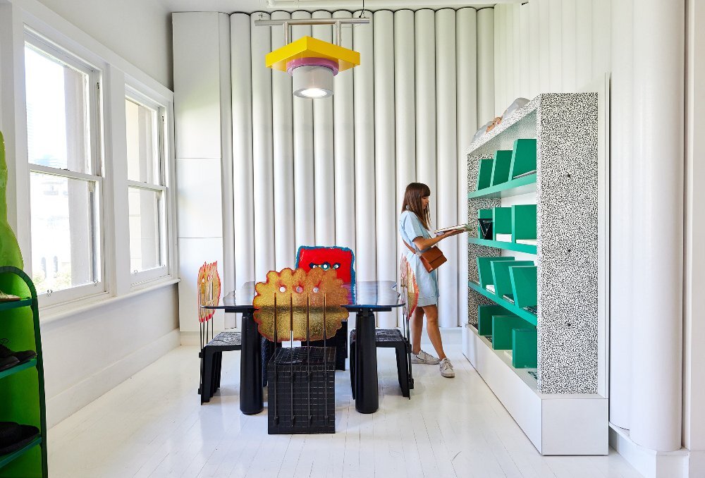 A woman is looking at books in a shop with white walls and flooring, and unique designer furniture.