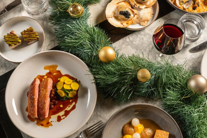 Several plates of food and smaller side dishes on a restaurant table, with a green Christmas tinsel and gold baubles as a table decoration.