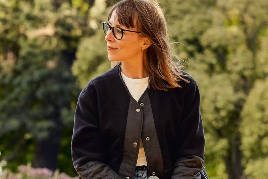 Acting coach, Kate Ellis, looking off to the side, with blurred greenery behind her.