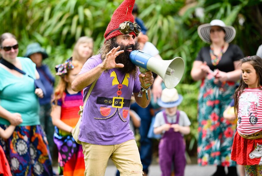 A man with a bushy beard dressed as a gnome addresses people with a loudspeaker. 