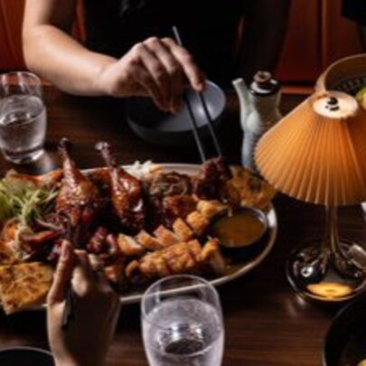 Hands of people tucking in to a Chinese banquet platter with a small table lamp.