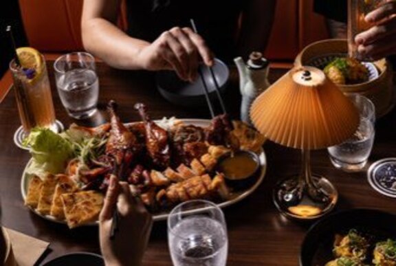 Hands of people tucking in to a Chinese banquet platter with a small table lamp.