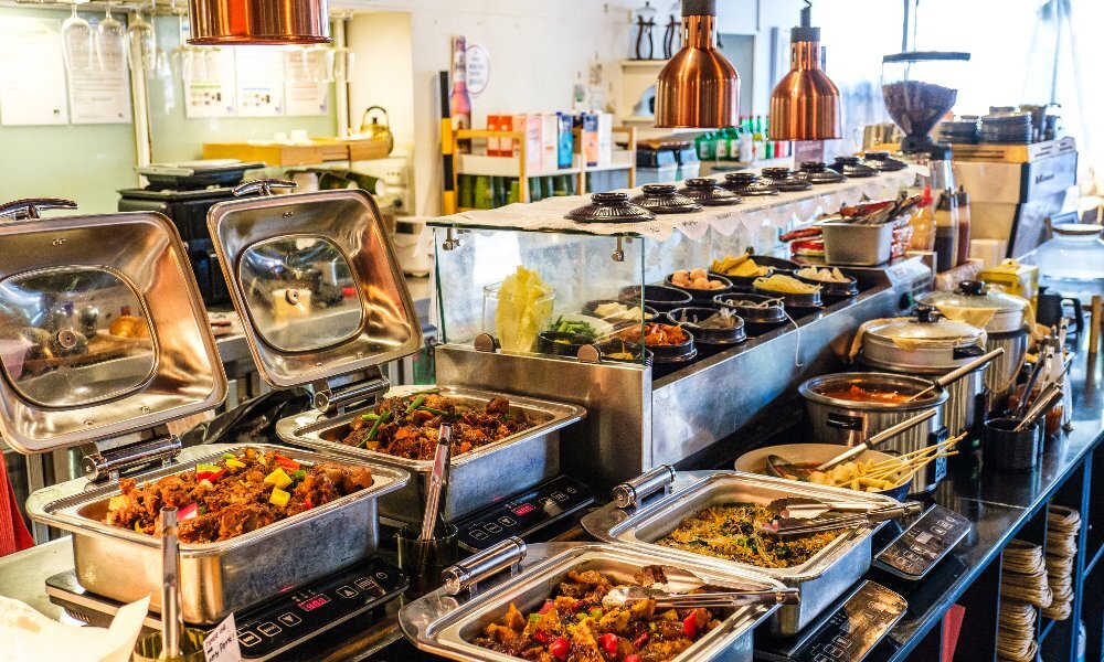 An array of bain-maries, hotpots and bowls filled with Korean food (japchae, fish cake soup, kimchi, dumplings etc.) in a cosy, warmly lit all-you-can-eat restaurant.