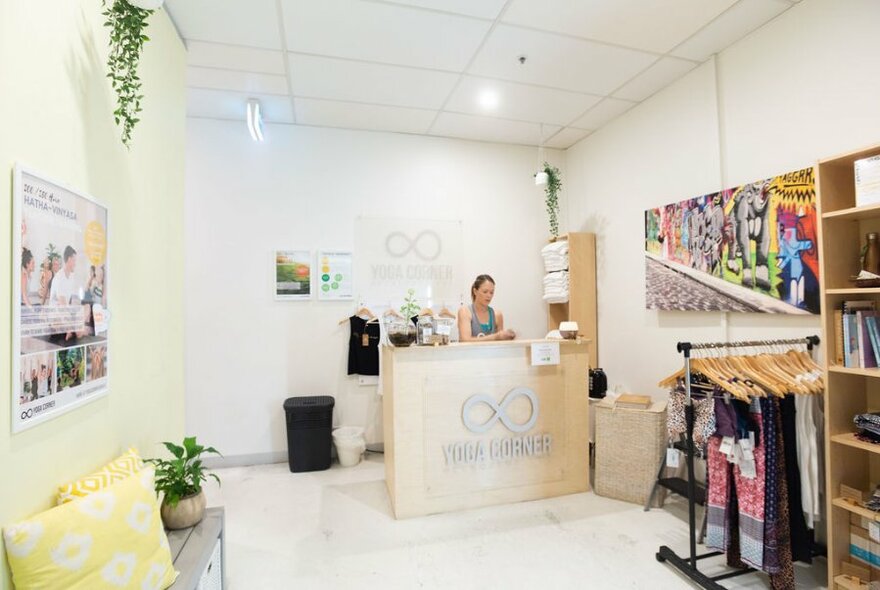 The reception area of Yoga Corner studio  showing a desk with person sitting behind it, shelves and a general waiting area.