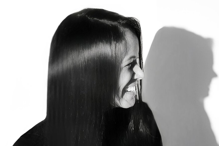 A smiling woman in profile, with long straight hair hanging over one side of her face; black and white.