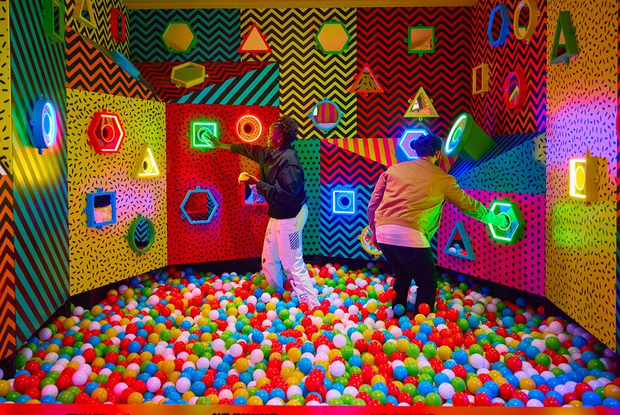 Two adults in a ball pit putting balls through the matching colour holes.
