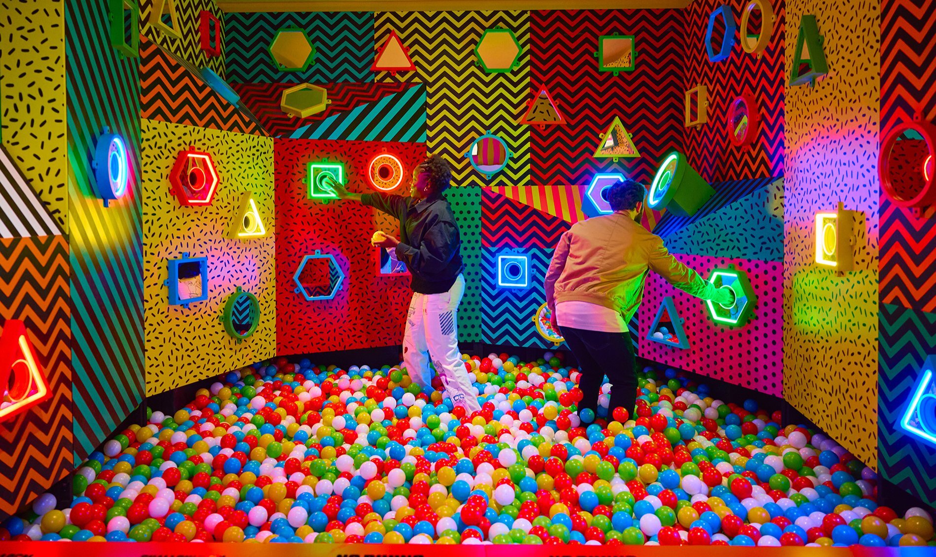 Two adults in a ball pit putting balls through the matching colour holes.