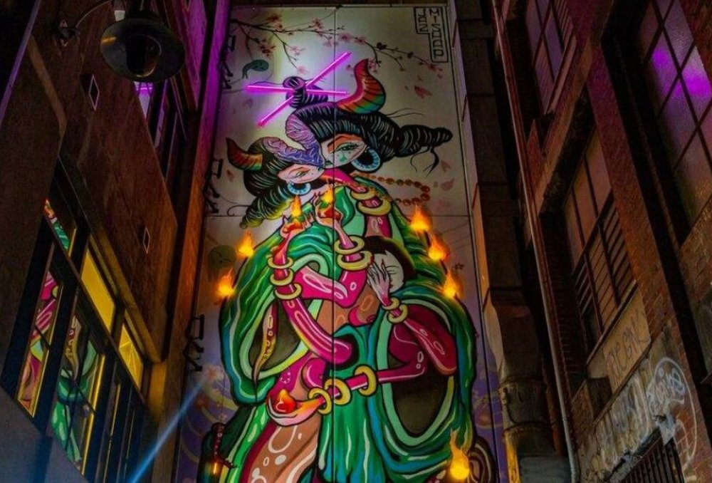 A mural of a strange glowing creature in a laneway.