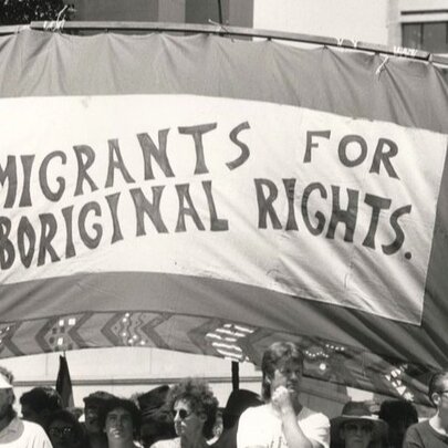 A protest banner from the 1960s with the slogan 'Migrants for Aboriginal Rights' and people marching underneath it.
