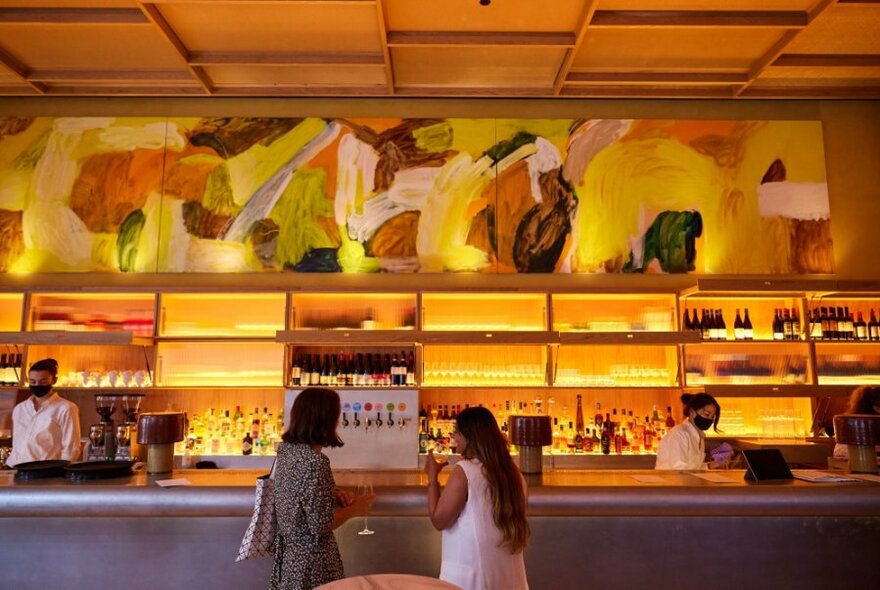 People getting a drink at a bar with yellow lighting. 