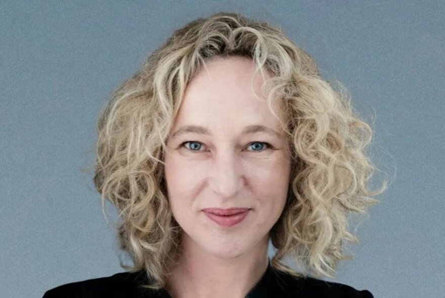 Portrait of broadcaster Sally Warhurst with a blue-grey background.