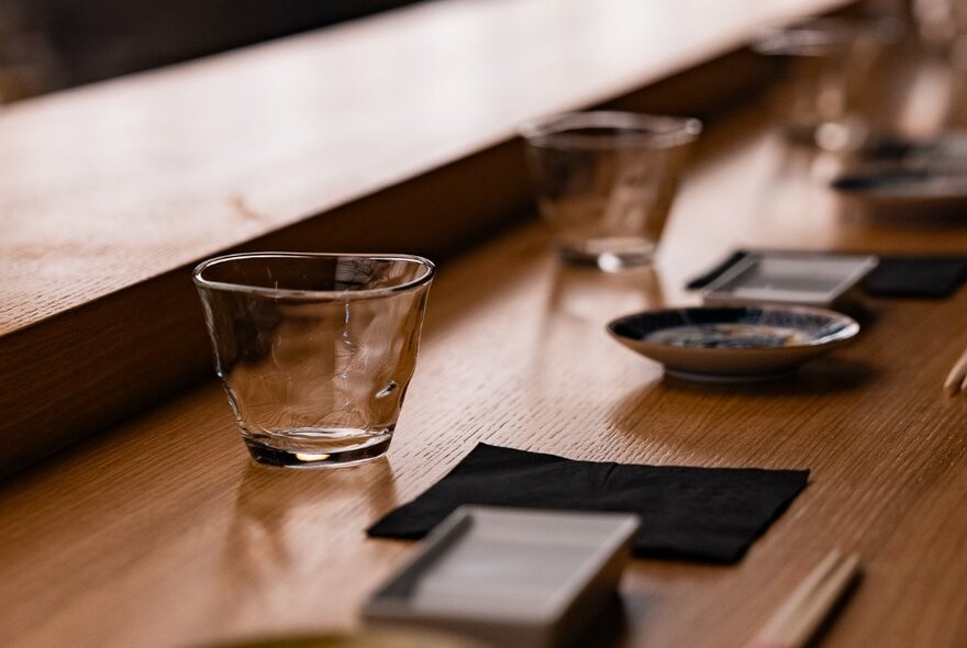 A sushi counter set twith glasses, dipping trays and chopsticks.