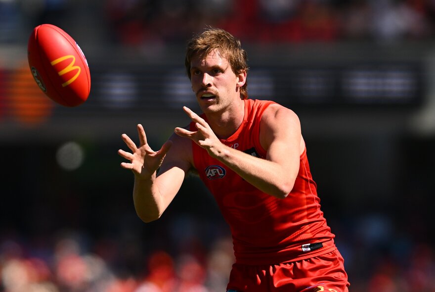 A Gold Coast AFL player about to mark a red football during a game.