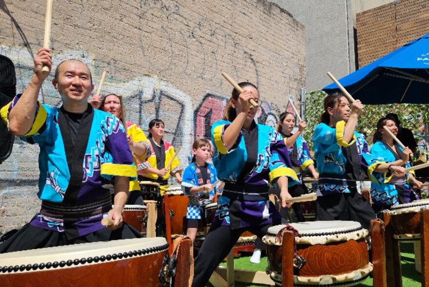 A group of Japanese drummers performing outside in teal blue colourful samurai-style costumes.