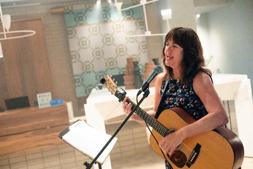 A solo singer with a guitar performing in an empty lobby space.