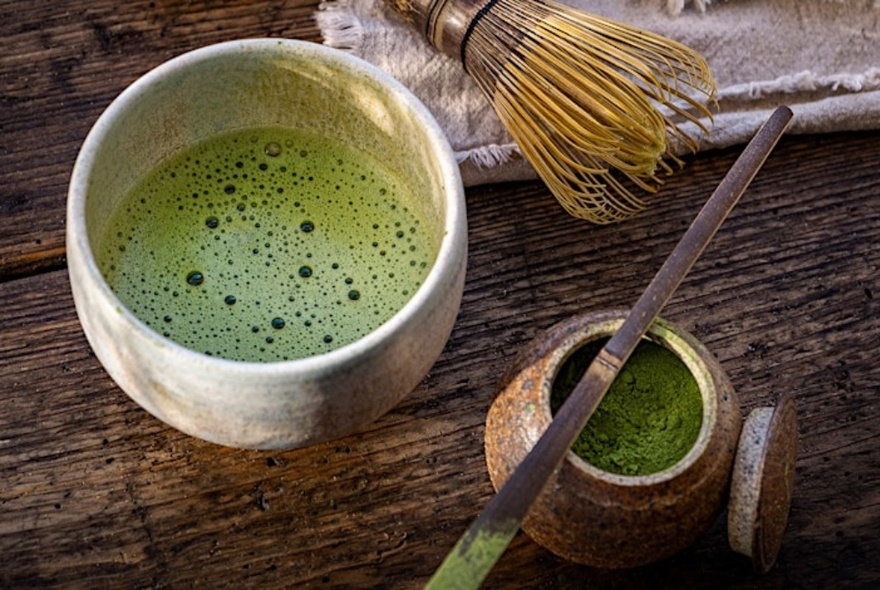 A traditional Japanese matcha tea in a handcrafted ceramic mug, with a small earthenware container of matcha powder alongside.