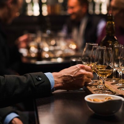 A forearm reaching out to select a glass from a whisky flight, in a bar setting.