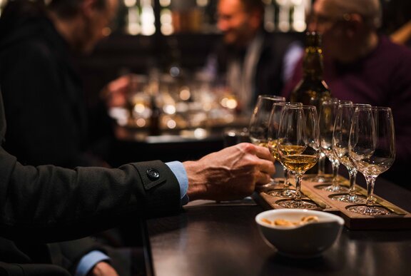 A forearm reaching out to select a glass from a whisky flight, in a bar setting.