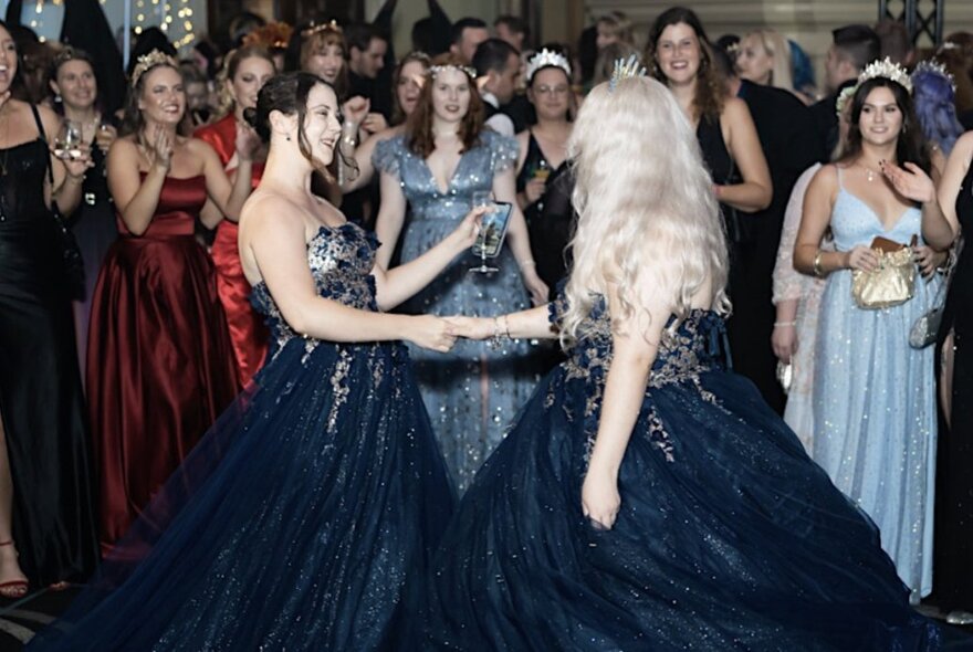 Two people wearing gowns dancing while a crowd in formal wear look on.