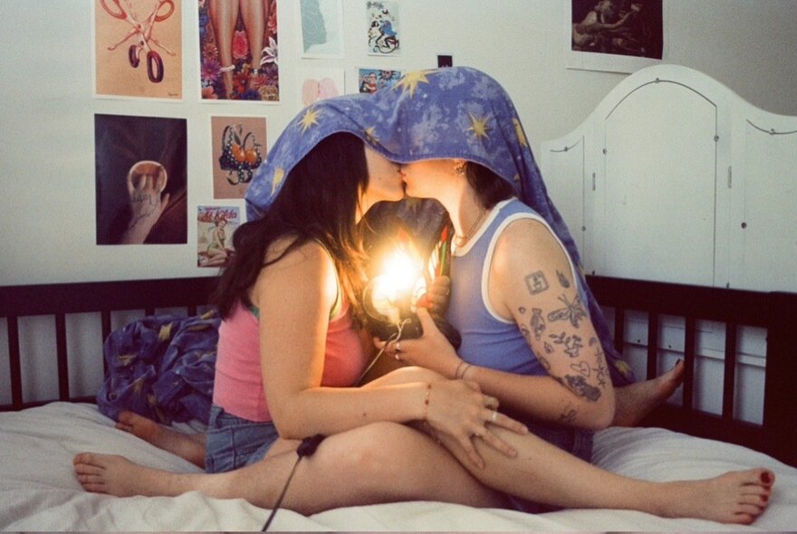 A couple kissing on a bed with a lamp, their heads covered with a towel.