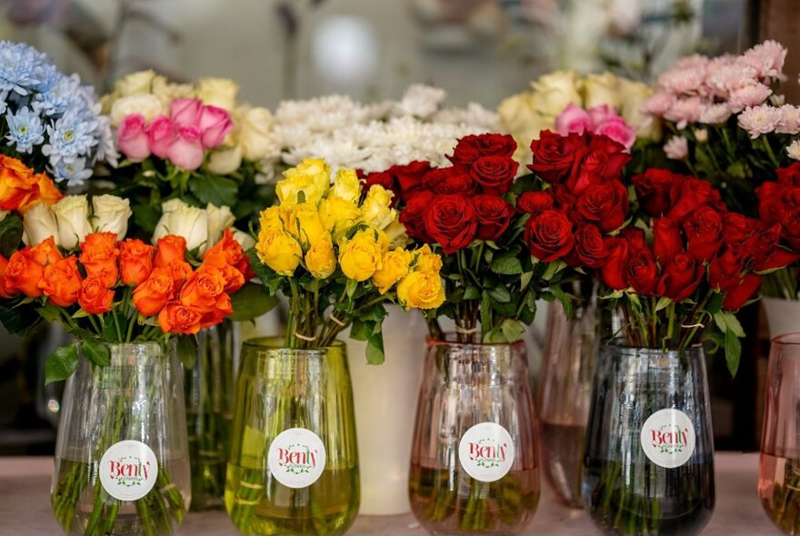 Vases of red, yellow, white and orange coloured roses at a florist shop.