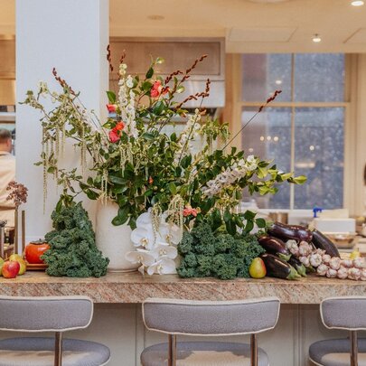 The bar counter at Hazel restaurant with piles of vegetables on display, a vase of flowers and kitchen staff in the background.