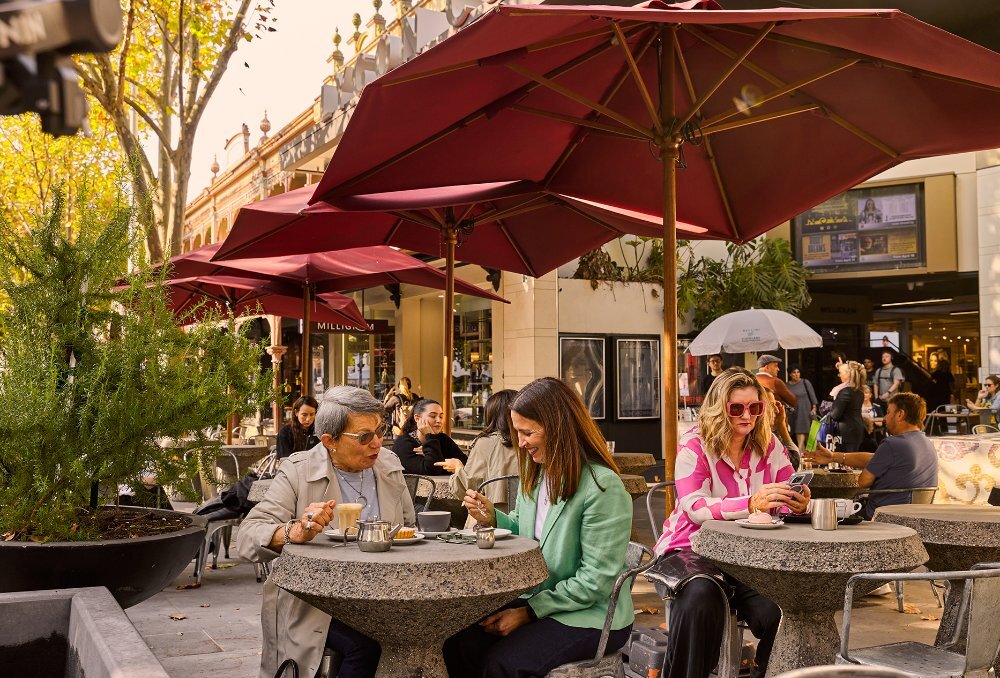 People dining outside on the street under red umbrellas at a cafe.