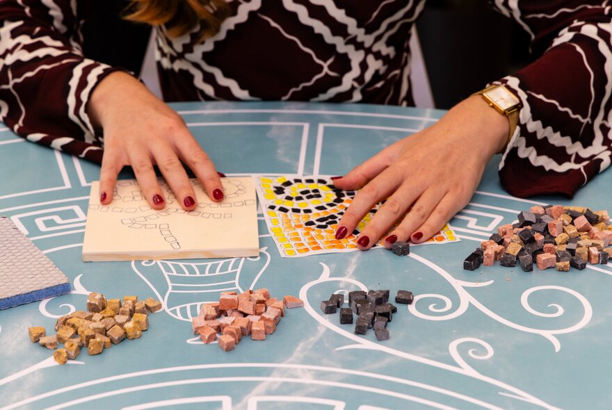 Hands with red nail polish doing a craft activity on a blue tablecloth.