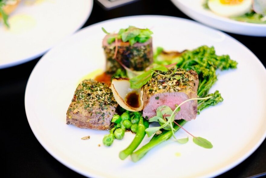 White dinner plate with a portion of seared beef fillet on a bed of green broccoli stems.