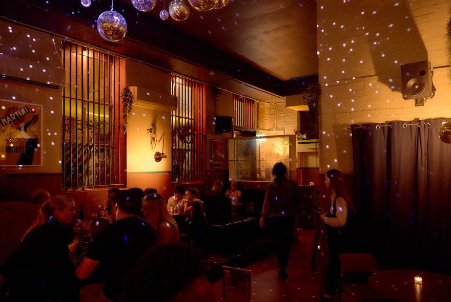 Interior of dimly lit Solace Bar with patrons drinking at tables, mirrored disco balls casting reflections on the ceiling and walls.