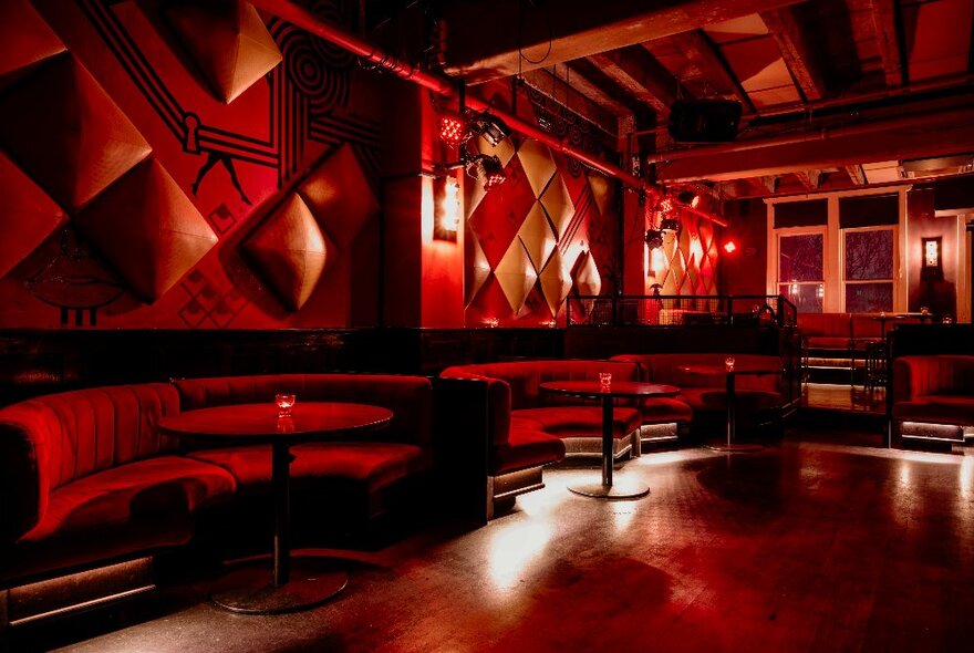 Red velvet booth seating at the bar The Toff in Town, with large windows behind the bar, and a reddish glow to the space.