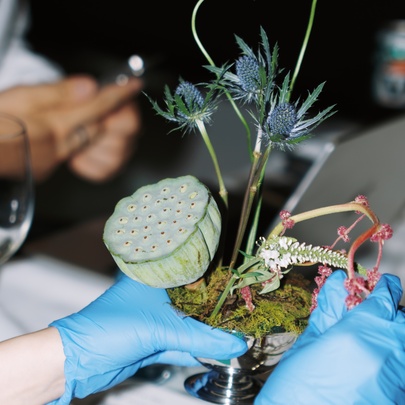 A person wearing blue rubber gloves creating an Ikebana arrangement, which is the traditional Japanese art of flower arranging.