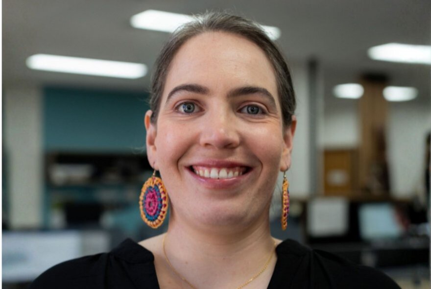 A woman with large tribal earrings smiling warmly in an office. 