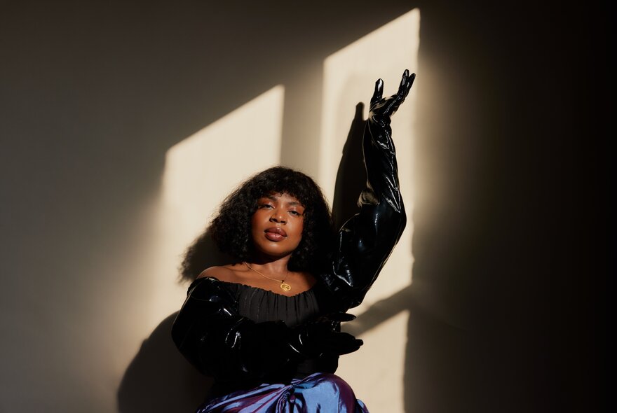 A female jazz musician posing in a glamorous ball gown with her left arm in the air.
