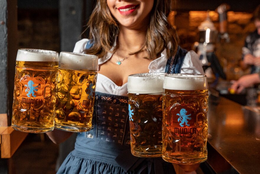 Waitress wearing a dirndl dress holding four large steins of beer.