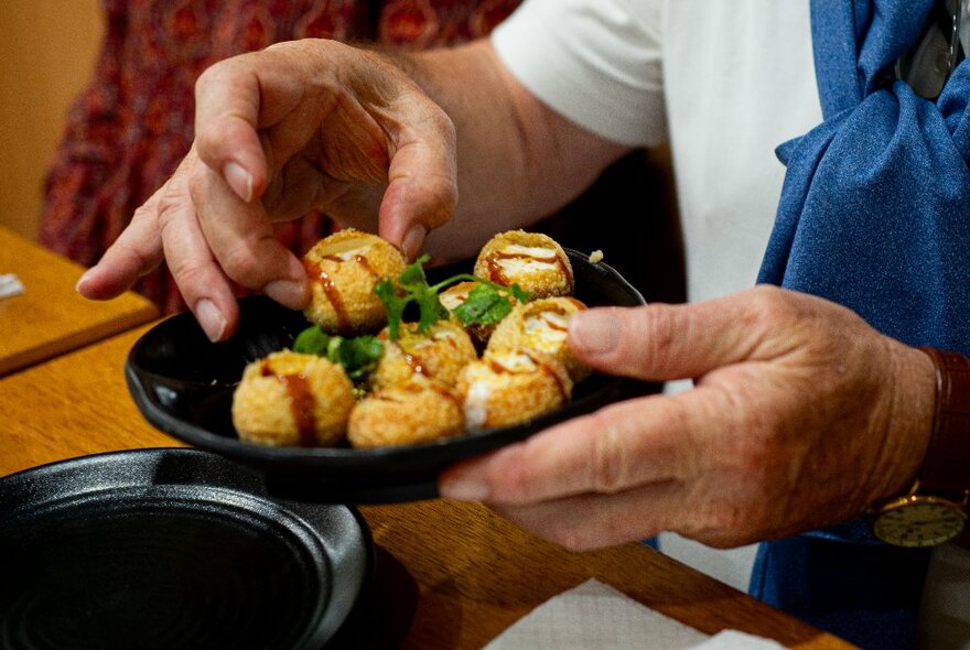 One hand holding a plate of round dumplings, while the person's other hand is picking one up.