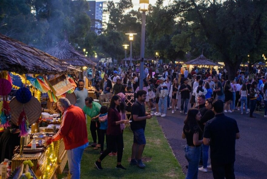 People milling around at an street food festival in a park, crowds milling around on the pavement and others lining up at food stalls.