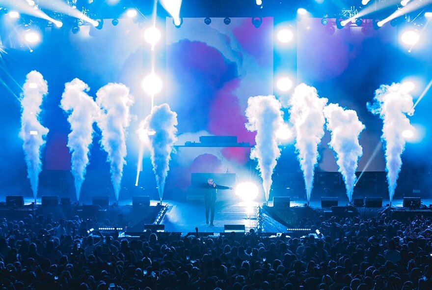 Plumes of smoke billowing from a blue-lit stage with bright lighting.