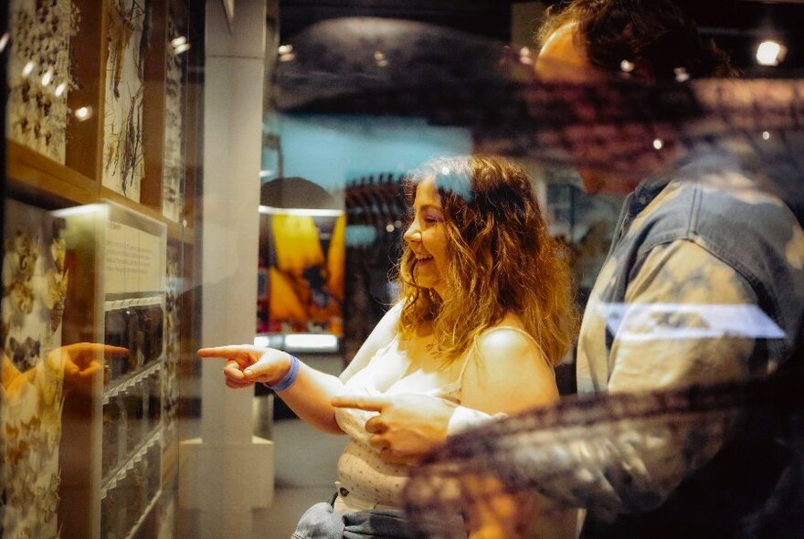 Two people looking and pointing to objects in a glass case on a museum wall.