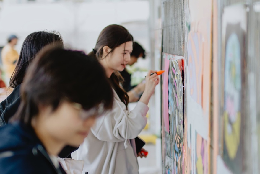 People drawing on artworks pinned to a wall.