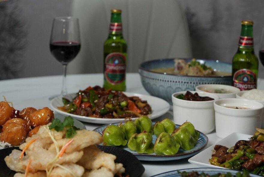 A table in a restaurant with plates of Chinese food including dumplings, beef stir-fry and small bottles of Chinese beer.