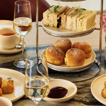 A high tea stand and various small plates with sandwiches, scones and small sweet and savoury bites, and two flutes of champagne.