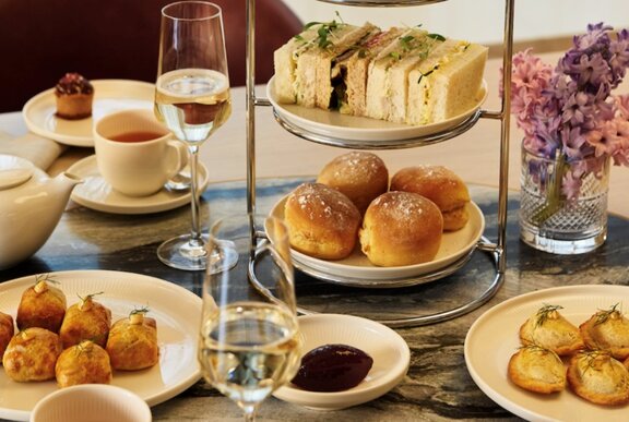 A high tea stand and various small plates with sandwiches, scones and small sweet and savoury bites, and two flutes of champagne.