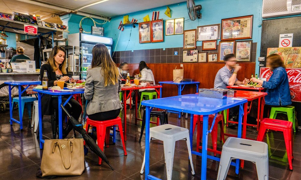 People dining at colourful tables in a casual Thai restaurant.